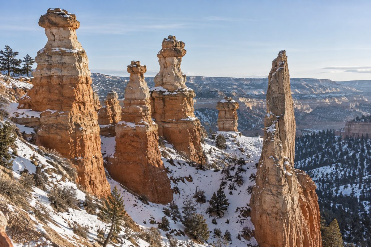 Orange and pale layered rock spires rise beside a thin rock fin, with scattered snow on ledges.